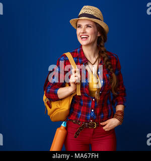 La ricerca di luoghi ispiratrice. Sorridendo viaggiatore attivo donna con zaino guardando in lontananza isolato su blu Foto Stock