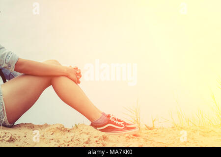 Donna seduta abbracciando le ginocchia con dolore. Foto Stock