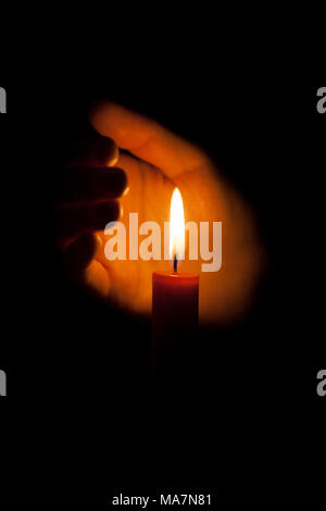 Una candela che brucia di notte, protetto dalla mano di una donna. Candela incandescente su sfondo scuro con spazio libero per il testo. Close up, dep poco profonda Foto Stock