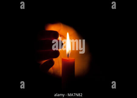 Una candela che brucia di notte, protetto dalla mano di una donna. Candela incandescente su sfondo scuro con spazio libero per il testo. Close up, dep poco profonda Foto Stock