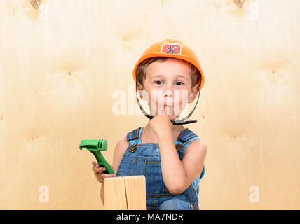 Kid boy come divertente builder tenendo premuto il dito in bocca dopo colpendolo con un martello Foto Stock