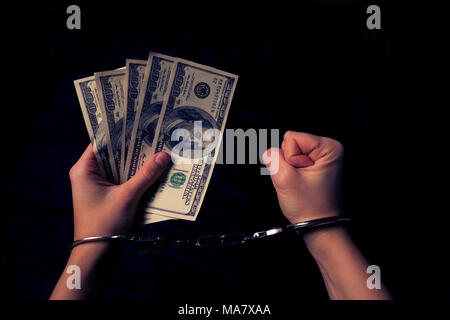 Le mani delle donne in manette con dollari nelle sue mani Foto Stock