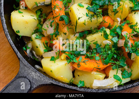 Patate fritte con le verdure con il prezzemolo tritato in una ghisa padella su una tavola di legno Foto Stock