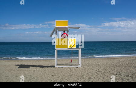 Un bagnino si affaccia al mare dalla sua cabina su una spiaggia deserta. Foto Stock