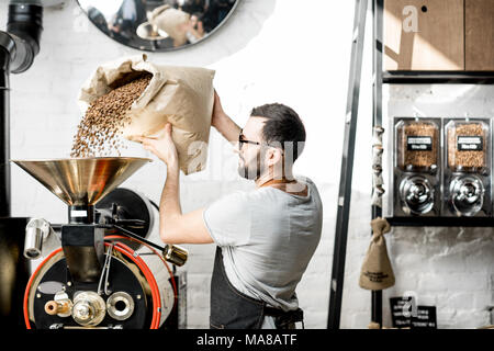 L'uomo versando i chicchi di caffè nel tostatore la macchina in ambienti chiusi Foto Stock