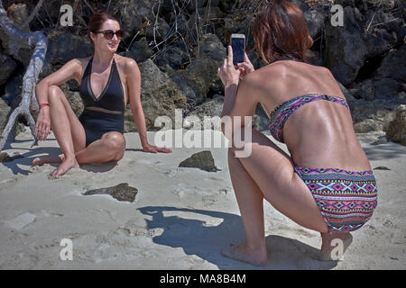 Donna di prendere una fotografia del suo amico femmina utilizzando uno smartphone. Donna bikini spiaggia. Foto Stock