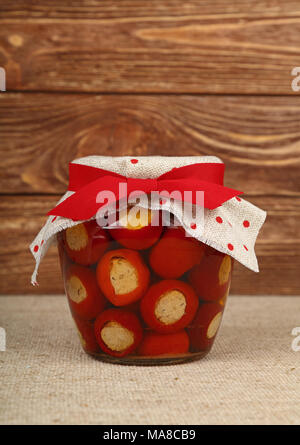 Close up di un vasetto di vetro di decapare red hot chili di ciliegia Peperoncini ripieni con soft di ricotta con tela di lino decorazione di coperchio e r Foto Stock