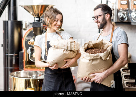 Ritratto di due baristi felice in uniforme in piedi con sacchi pieni di chicchi di caffè presso il negozio di caffè Foto Stock