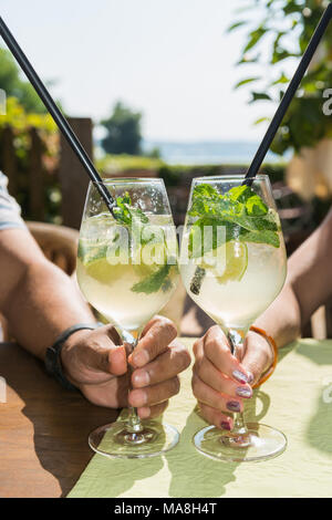 Giovane bere cocktail mojito in un accogliente bar all'aperto sulla spiaggia. Vecchia mano maschio e la mano di una giovane donna sono tenendo gli occhiali. Foto Stock