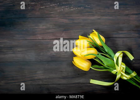 Bouquet di tulipani gialli con nastro giallo su vintage in legno scuro dello sfondo della tabella. vacanze concetto. Copia dello spazio. Foto Stock