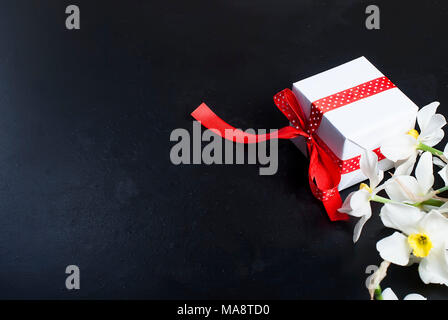 Vista superiore mazzo di narcisi e confezione regalo con nastro rosso su sfondo nero. Fiori il concetto di sfondo spazio copia Foto Stock