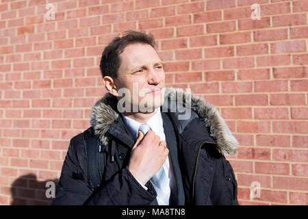 Bello e attraente giovane serio infelice imprenditore di poppa closeup volto ritratto in piedi di fronte a un muro di mattoni, fascetta di fissaggio, in tuta e cravatta su int Foto Stock