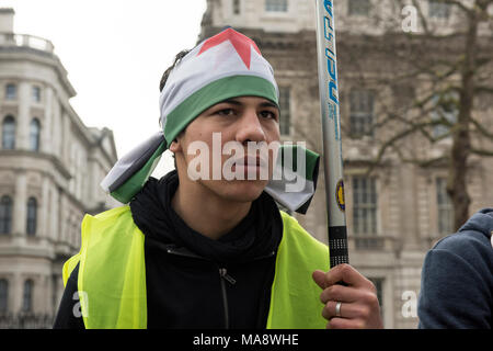 Un giovane uomo siriano, indossa una bandiera siriana sopra la testa, sta protestando contro il regime di Assad al di fuori di Downing Street a Londra, Regno Unito. Foto Stock