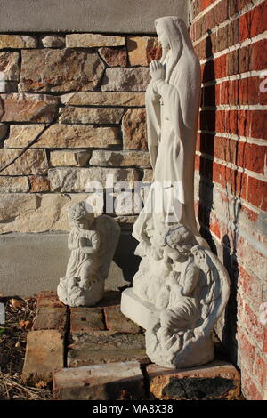 Una collezione di statue di cemento del cristianesimo la Vergine Maria orante con due angeli di fronte a una casa. Foto Stock