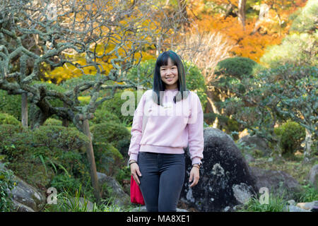 Giovane ragazza asiatica in piedi in un giardino giapponese nel fogliame di autunno Foto Stock