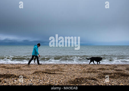 Slapton Sands, South Devon 30 marzo 2018. Una donna cammina il suo cane lungo un umido e ventoso spiaggia a Slapton, South Devon. (C) Paolo Swinney/Alamy Live News Foto Stock