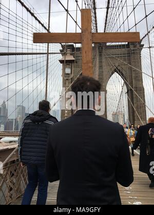 Un giovane adulto porta una croce attraverso il ponte di Brooklyn a New York come parte delle processioni annuali di Venerdì Santo e Pasqua e delle stazioni della Croce Foto Stock