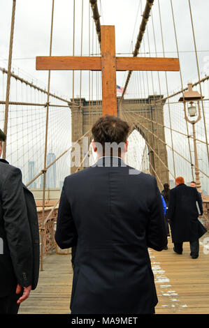 New York, NY, STATI UNITI D'AMERICA MARZO 30, 2018 Un giovane uomo porta una croce di legno attraverso il Ponte di Brooklyn, come parte di una processione del Venerdì Santo a New York Credito: James Kirkikis/Alamy Live News Foto Stock
