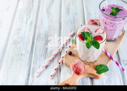 Due estivo rinfrescante rosa e viola o frullato frullato con la menta, lo yogurt, mirtilli e fragole. in vetro con ingredienti, su bianco woode Foto Stock