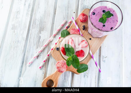 Due estivo rinfrescante rosa e viola o frullato frullato con la menta, lo yogurt, mirtilli e fragole. in vetro con ingredienti, su bianco woode Foto Stock