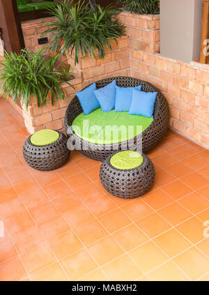 Divano armatura bastone di rattan sedie con cuscini blu sulla piastrella arancione e il vecchio muro di mattoni Foto Stock