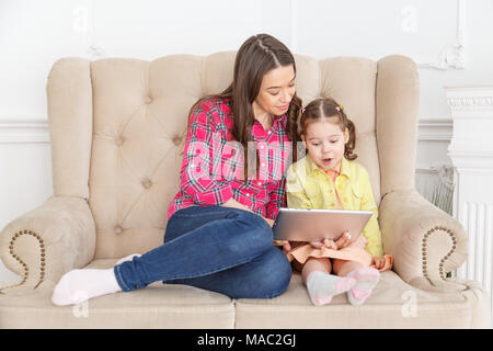 Madre e figlia sul divano di casa e giocare con il tablet pc insieme Foto Stock