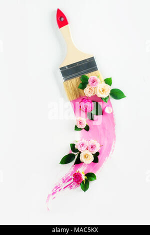 Molla creativa trasfigurazione concetto con fiori, spazzola di vernice e un swoosh di colore rosa. Tasto alto concetto decor con copia spazio. Foto Stock