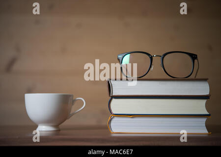 Bicchieri sulla pila di libri e una tazza di caffè sul tavolo di legno. Il concetto di istruzione. Foto Stock