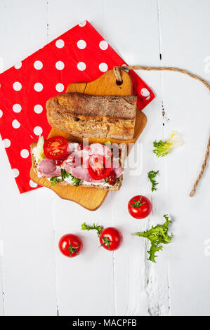 La ciabatta in sandwich con prosciutto, pomodori ciliegini e insalata di bianco su uno sfondo di legno. Foto Stock