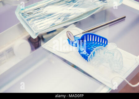 Set di confezionati sterilizzati attrezzature mediche strumenti, dentista 's mirrow e stampi a ganascia sulla maschera sul tavolo di lavoro in clinica ortodontica. Messa a fuoco selettiva, spazio per il testo. Foto Stock