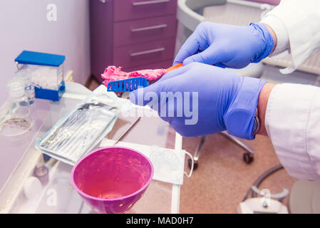 Vista ravvicinata del dentista le mani tenendo un modello di ganasce e mettere la soluzione di silicone per impronta dentale. Denti impressioni , odontotecnico concetto. Messa a fuoco selettiva, spazio per il testo. Foto Stock