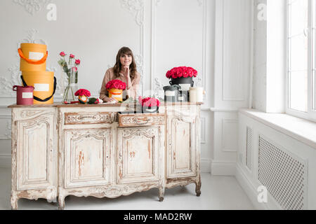 Giovane donna fioraio disponendo le piante nel negozio di fiori. Persone, business vendita fiorai e concetto. Bouquet di rose rosse Foto Stock