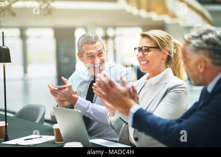 Gruppo di imprenditori matura seduti ad un tavolo in un ufficio moderno battendo le mani durante una presentazione Foto Stock