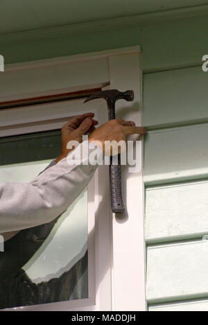 Close up di un uomo con le mani in mano tenendo un martello come egli in installa una nuova finestra e schermo in una giornata di sole Foto Stock