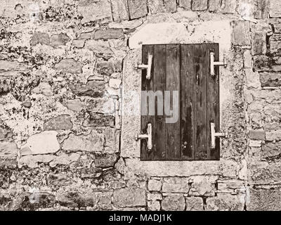 Finestra con finestra chiusa persiane in una parete di roccia ruvida Foto Stock