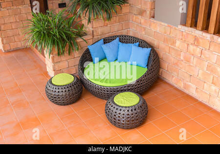 Divano armatura bastone di rattan sedie con cuscini blu sulla piastrella arancione e il vecchio muro di mattoni Foto Stock