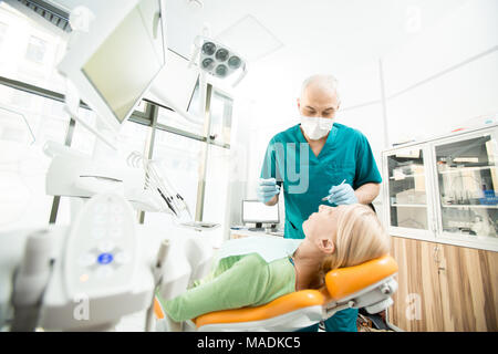 Donna matura giacente sulla poltrona del dentista mentre andando a controllare la sua cavità orale in cliniche Foto Stock