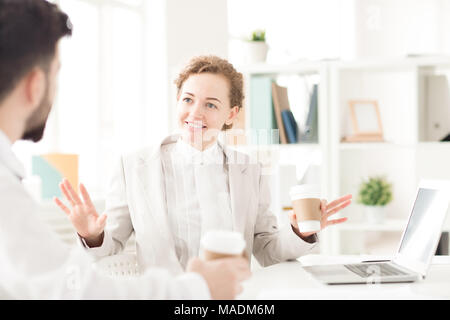 Sorridente imprenditrice a discutere di lavoro in occasione di una riunione e di bere il caffè Foto Stock