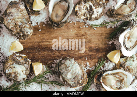 Fresche appena aperto le ostriche e la fetta di limone su rustico sfondo di legno Foto Stock