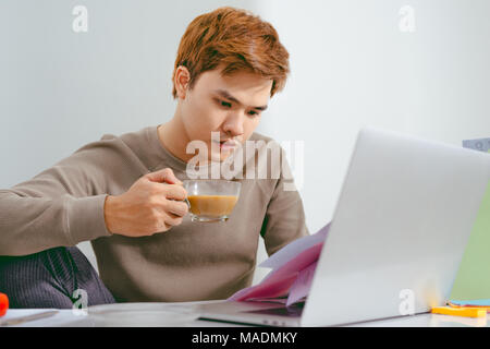 Giovane uomo triste analizzando le finanze di casa mentre gesticolando con la mano e guardando i documenti. Seduto vicino a tavola con tablet. Foto Stock