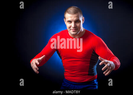 Un forte dai capelli scuri sportman in un rosso di indossare abbigliamento sportivo rush che pongono riparo contro un blu a luci su un isolato nero lo sfondo Foto Stock