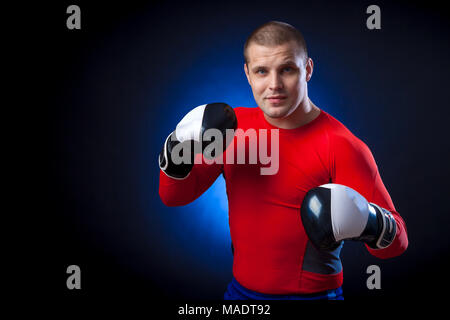 Un forte dai capelli scuri boxer sportman in un rosso di indossare abbigliamento sportivo rush guard e in bianco e nero i Guantoni boxe contro un blu a luci su un nero i Foto Stock