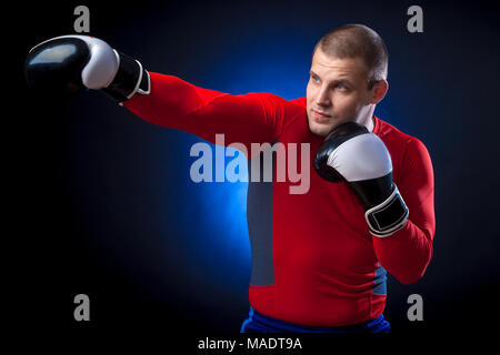 Un forte dai capelli scuri boxer sportman in un rosso di indossare abbigliamento sportivo rush guard e in bianco e nero i Guantoni boxe contro un blu a luci su un nero i Foto Stock