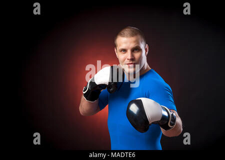 Un forte dai capelli scuri boxer sportman in un blu di indossare abbigliamento sportivo rush guard e in bianco e nero i Guantoni boxe contro un rosso a luci su un nero i Foto Stock