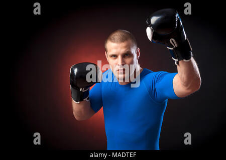 Un forte dai capelli scuri boxer sportman in un blu di indossare abbigliamento sportivo rush guard e in bianco e nero i Guantoni boxe contro un rosso a luci su un nero i Foto Stock