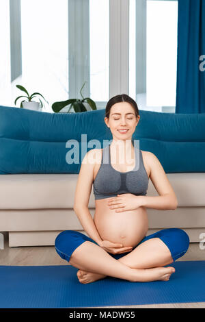 Felice donna incinta facendo esercizi yoga a casa. Donna incinta medita. Gravidanza gravidanza, yoga, uno stile di vita sano concetto Foto Stock