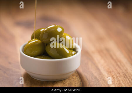 Big green olive salate in bianco ciotola sul tavolo di legno, fuoco poco profonda Foto Stock