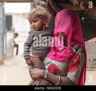 Donna con il suo capo coperto da una sciarpa rosa detiene un giovane bambino in un tradizionale villaggio vicino a Shapura, Rajasthan, India. Foto Stock