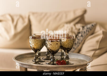 Il tiramisù in eleganti occhiali sul round tavolo in metallo con interni in beige. Composizione orizzontale. Profondità di campo ridotta. Foto Stock