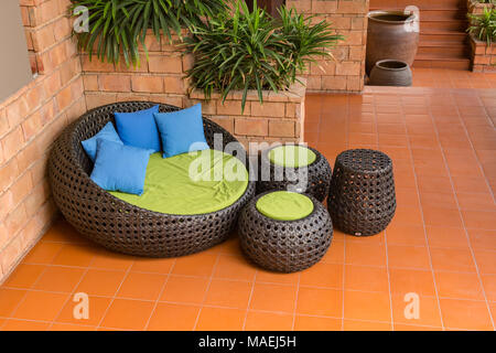 Divano armatura bastone di rattan sedie con cuscini blu sulla piastrella arancione e il vecchio muro di mattoni Foto Stock